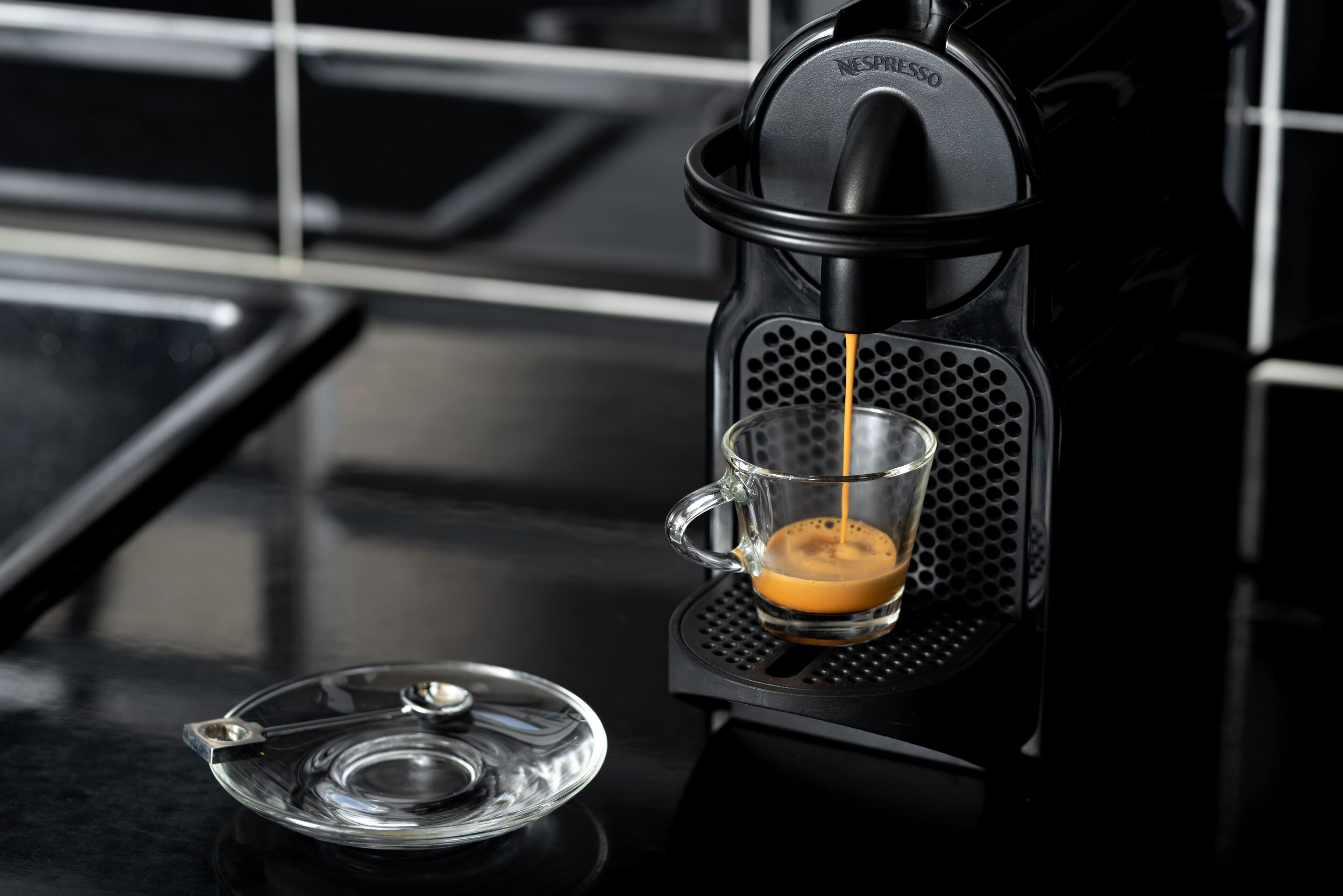 A Nespresso coffee machine dispensing espresso into a clear glass cup.