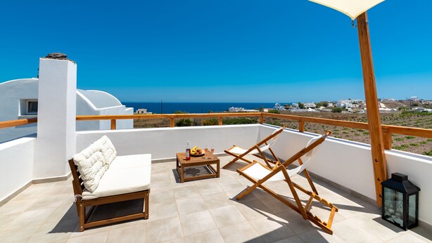 A balcony with a white cushioned sofa, wooden chairs, a small table with drinks, and a lantern. - Fully equipped house! (Santorini)