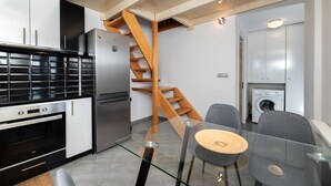 A compact kitchen with modern appliances, a glass dining table, and a wooden staircase. - Fully equipped house! (Santorini)