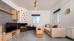 A modern living room with a fireplace, a flat-screen TV, a beige sofa, and a wooden coffee table. - Fully equipped house! (Santorini)
