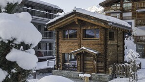 Un chalet en bois doté d’un balcon, entouré d’arbres et de montagnes couverts de neige.