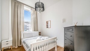 A bedroom with a bed, a dresser, a nightstand, a window with curtains, a chandelier, and a wall-mounted light. - Cozy, cute flat in Notting Hill - Pass the Keys (London)