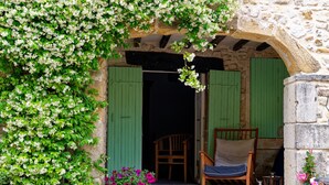 A stone building with green shutters, a wooden chair, and a potted plant. - Mastignac (Valreas)