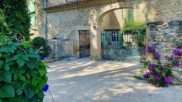 A stone building with a rustic entrance, a gravel driveway, and lush greenery. - Mastignac (Valreas)