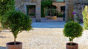 A stone building with an arched entrance, potted trees, and a gravel courtyard. - Mastignac (Valreas)