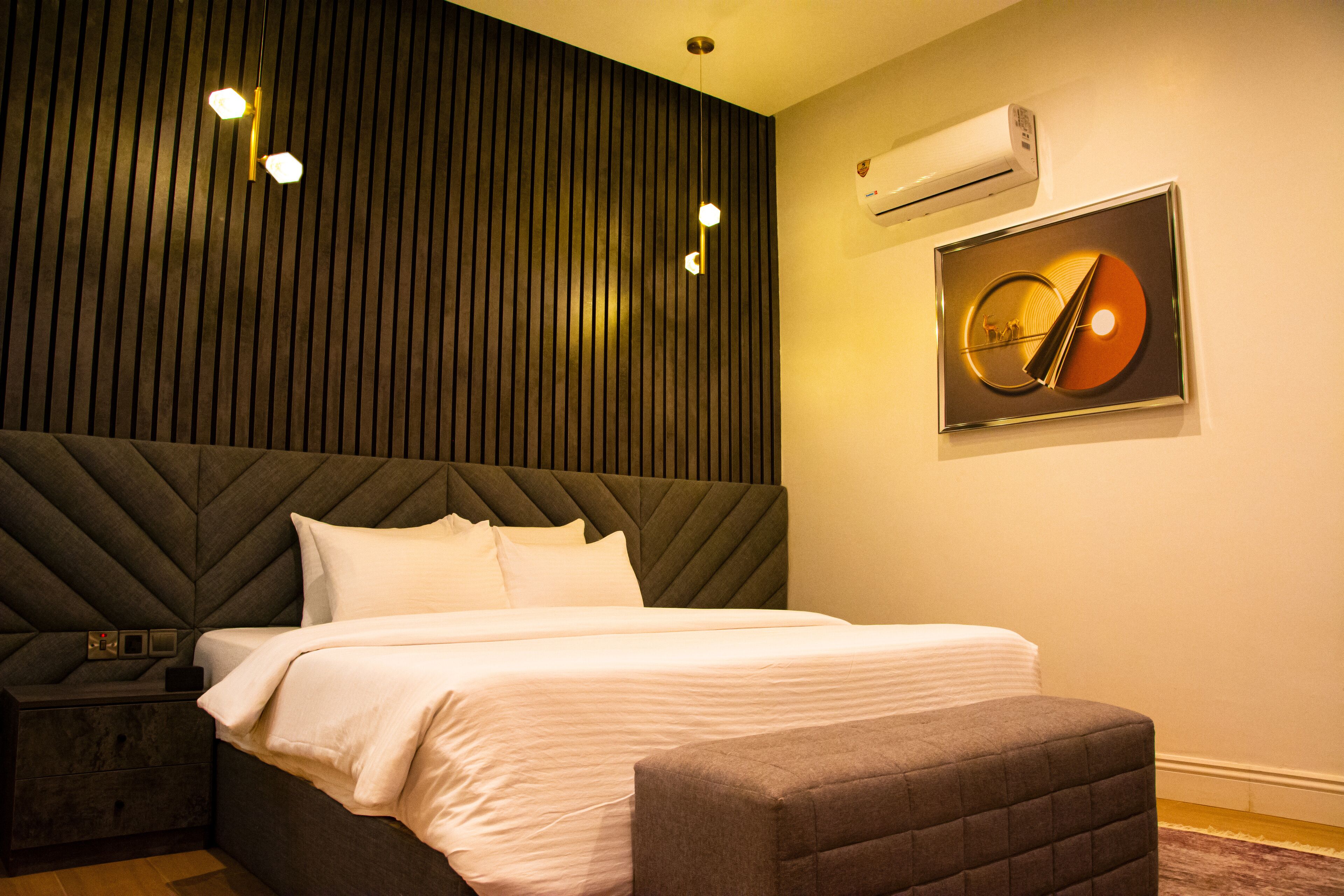 Een moderne hotelkamer met een groot bed, een hoofdbord met verticale lijnen, een klein nachtkastje en een wandairconditioner.