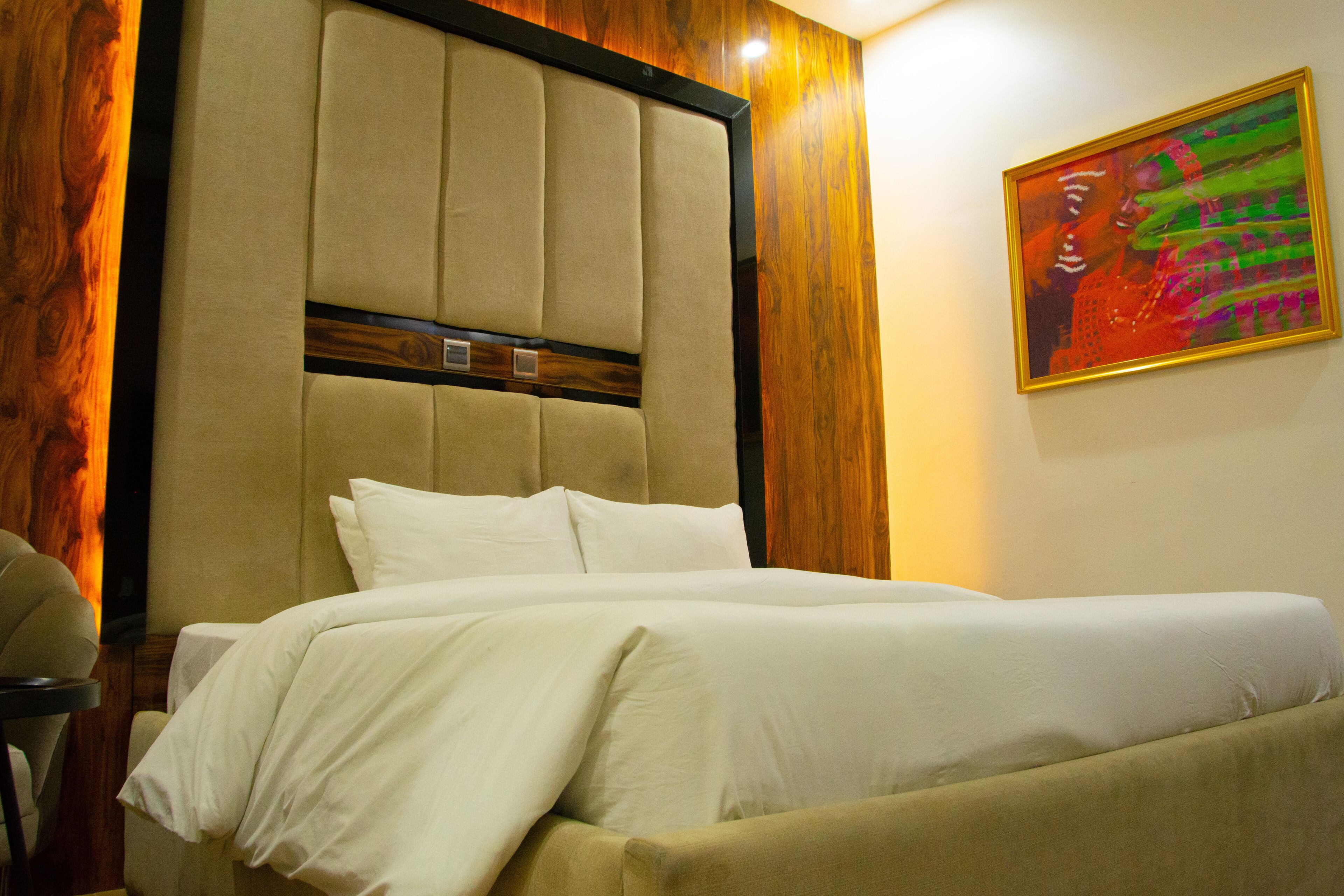 Una habitación de hotel con una cama grande, cabecera de madera y un cuadro en la pared.
