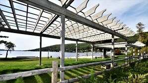 Ein überdachter Außenbereich mit Holzlattenzaun und Blick auf einen See und Hügel im Hintergrund.