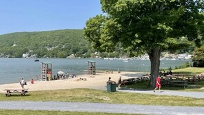 Ein Park am Seeufer mit Picknicktischen, einem Rettungsschwimmturm und einem Gehweg.