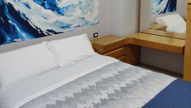 Ein Hotelzimmer mit einem Bett, einem Holztisch, einem großen abstrakten Gemälde und einem Spiegel.