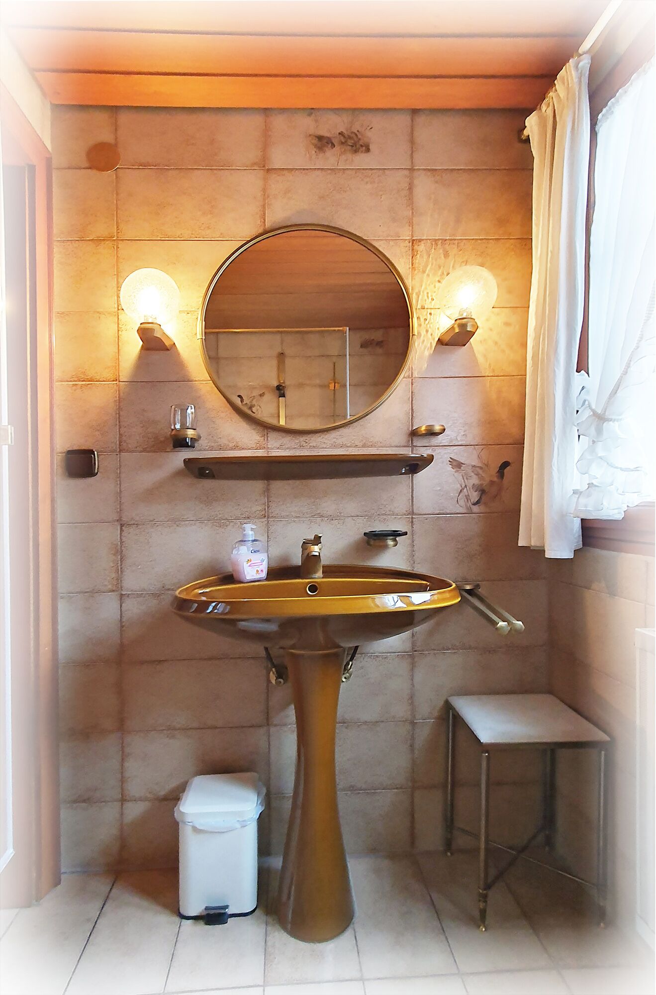 A bathroom with a pedestal sink, a round mirror, and two wall-mounted lights.