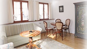 Un salon comprenant un canapé, une table à manger, des chaises, un meuble décoratif et une fenêtre avec des rideaux.