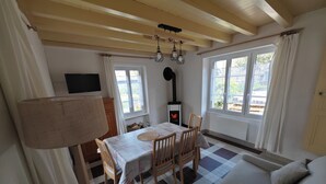 Una habitación acogedora con piso a cuadros, un sofá, una mesa de comedor con sillas, un televisor y un estufa de leña.