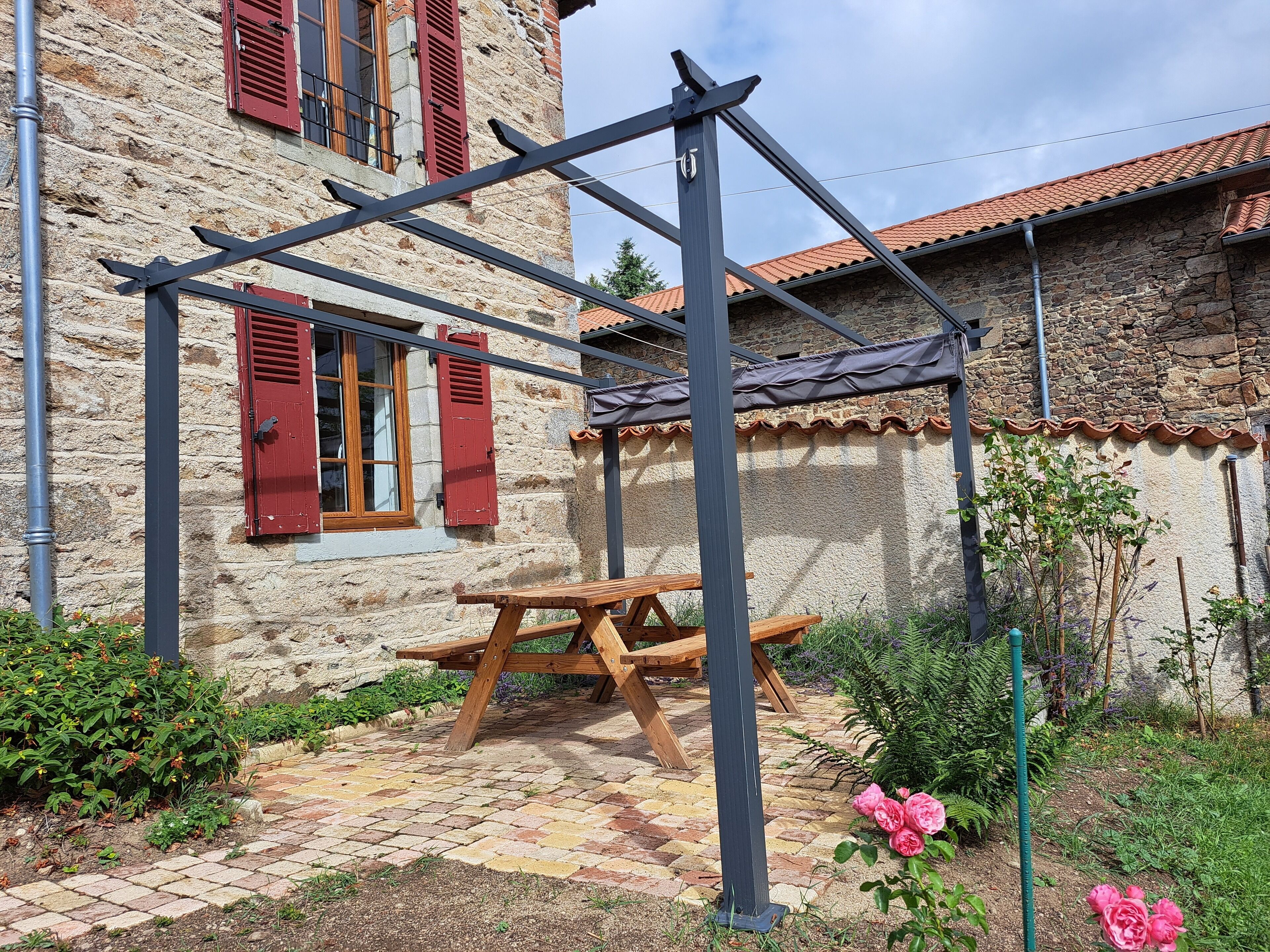 A stone building with red shutters, a wooden bench, and a pergola structure.