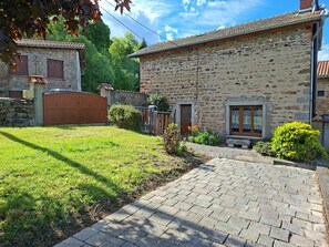 A stone building with a paved driveway, a wooden gate, and a small garden area.