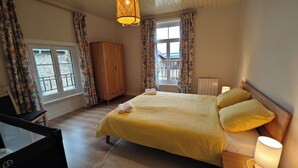 Un dormitorio con una cama, dos lámparas de noche, un armario de madera y un ventanal con cortinas.
