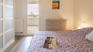 Quarto com cama, cômoda, radiador e porta para uma varanda.