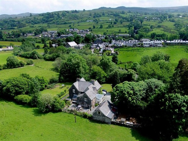 A rural village with stone houses, lush green fields, and rolling hills in the background.