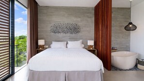 A modern bedroom with a large bed, a wall-mounted light fixture, and a view of greenery outside.