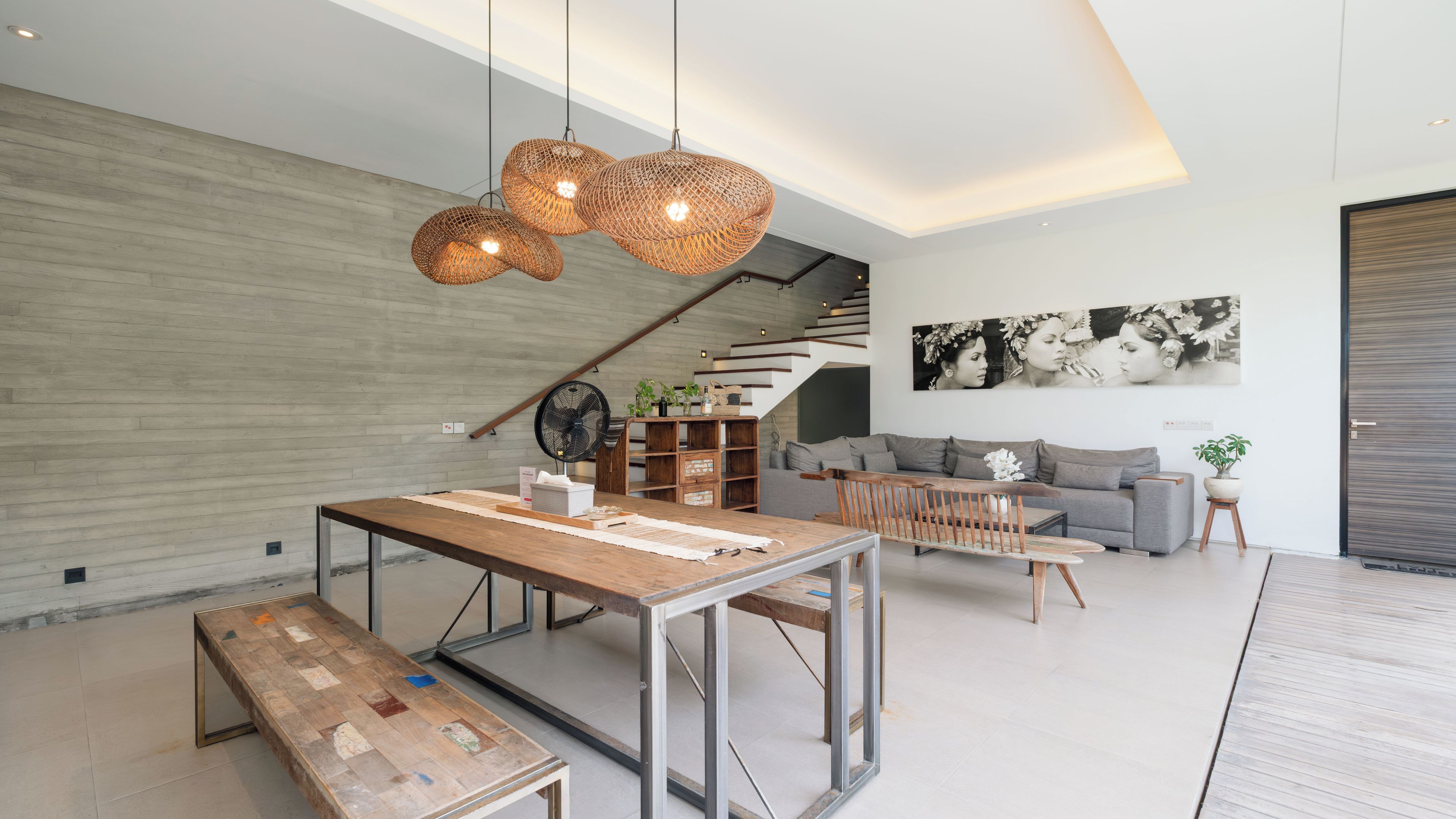 A modern living space with a dining area, a sofa set, a staircase, and a large artwork on the wall.