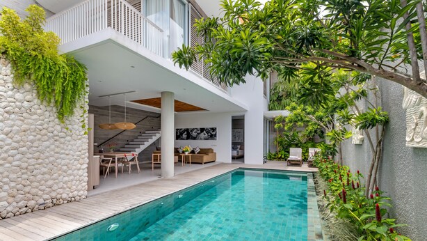 A modern outdoor pool area with a stone wall, wooden deck, and a staircase leading to an upper level. - Swan Villa R (Seminyak)