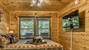 Una habitación de cabaña acogedora, con una cama, un televisor en la pared y una ventana con persianas.