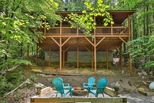 Une cabane dot ée d’une terrasse en bois et d’un foyer, entourée d’une forêt.