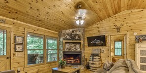 L’intérieur d’une cabane avec des murs en bois, une cheminée en pierre, un téléviseur et des tableaux encadrés.