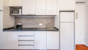 Eine moderne Küche mit weißen Schränken, einer Edelstahl-Spüle, einer Mikrowelle und einem Kühlschrank.