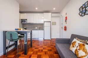 A compact living space with a kitchenette, a dining area, and a sofa with a cushion.