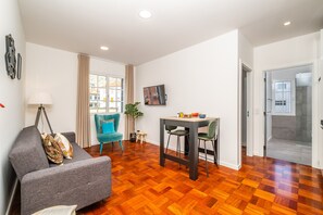 Un salon moderne comprenant un canapé, un fauteuil turquoise, une table à manger et un petit tabouret.