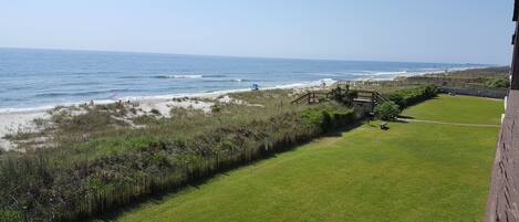 A grassy area with a wooden fence, a beach, and a pier in the distance.