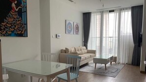 Un salon moderne avec une table à manger en verre, un canapé beige et une grande fenêtre agrémentée de rideaux.