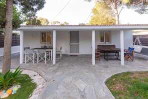 A covered patio area with stone flooring, a table with chairs, and a bench.