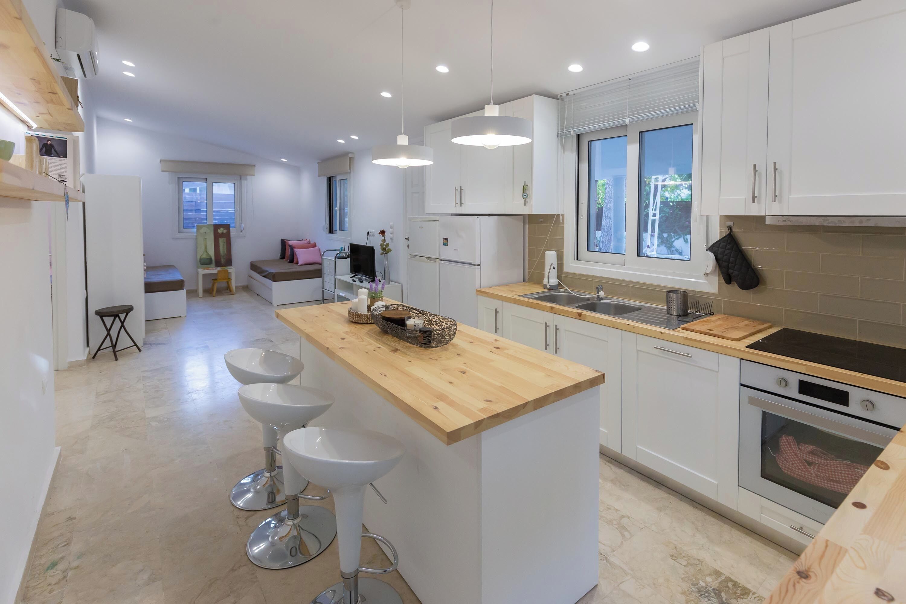 A modern kitchen with white cabinets, a wooden island with bar stools, a sink, and an oven.