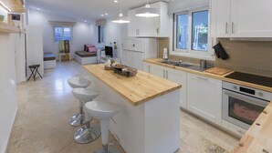 Une cuisine moderne avec des meubles blancs, un îlot central en bois doté de tabourets, un évier et un four.