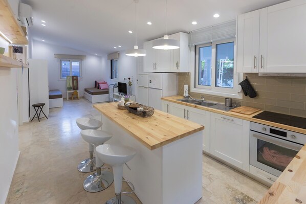 A modern kitchen with white cabinets, a wooden island with bar stools, a sink, and an oven.
