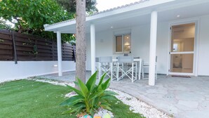Un espace patio agrémenté d’une clôture blanche, d’un arbre, d’un petit jardin avec des pierres peintes et d’une table avec des chaises.