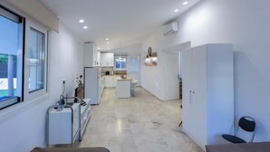 Une chambre d’hôtel moderne avec un lit, un petit bureau, une chaise, une fenêtre et, au fond, une kitchenette.