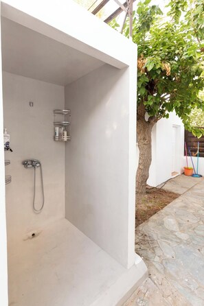 A modern outdoor shower with a metal hose and a shelf, a tree, and a stone pathway.