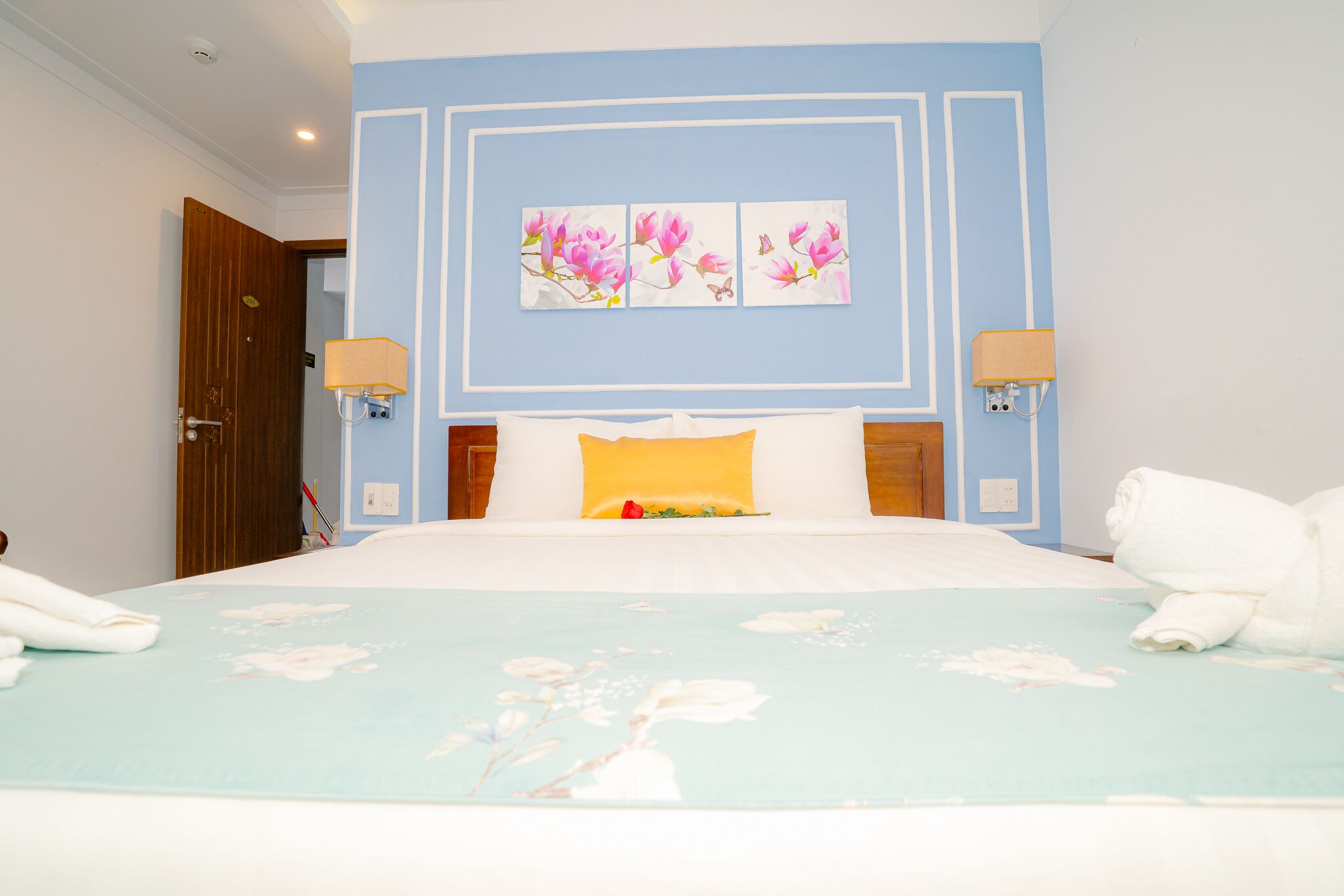 A hotel room with a bed, two wall-mounted lamps, a floral bedspread, and a door.