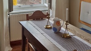 Une pièce avec une table et des chaises en bois, une fenêtre avec des rideaux, un radiateur et une vue sur des maisons et des montagnes.