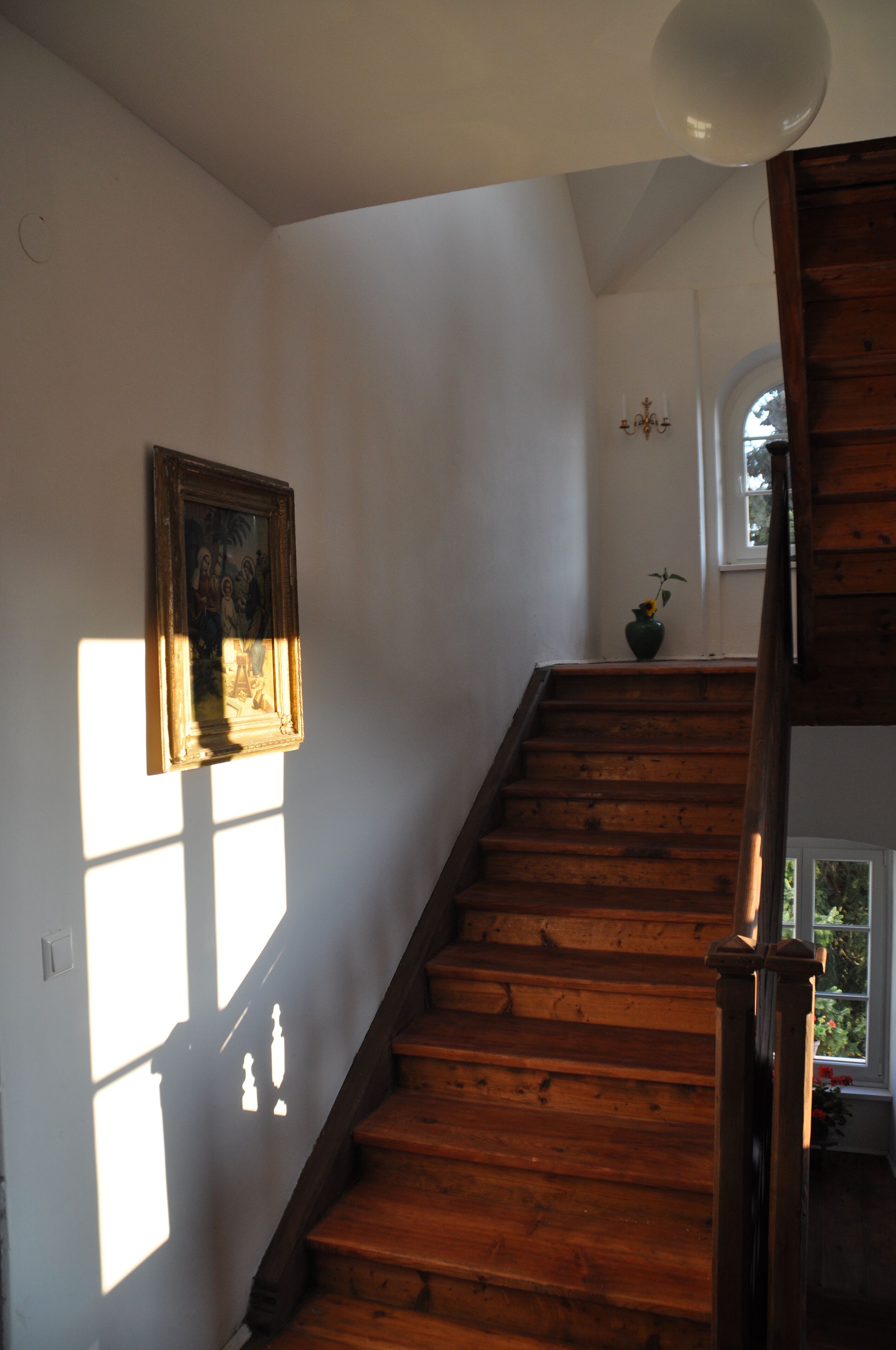 Una escalera de madera con un cuadro en la pared y un jarrón con una planta.