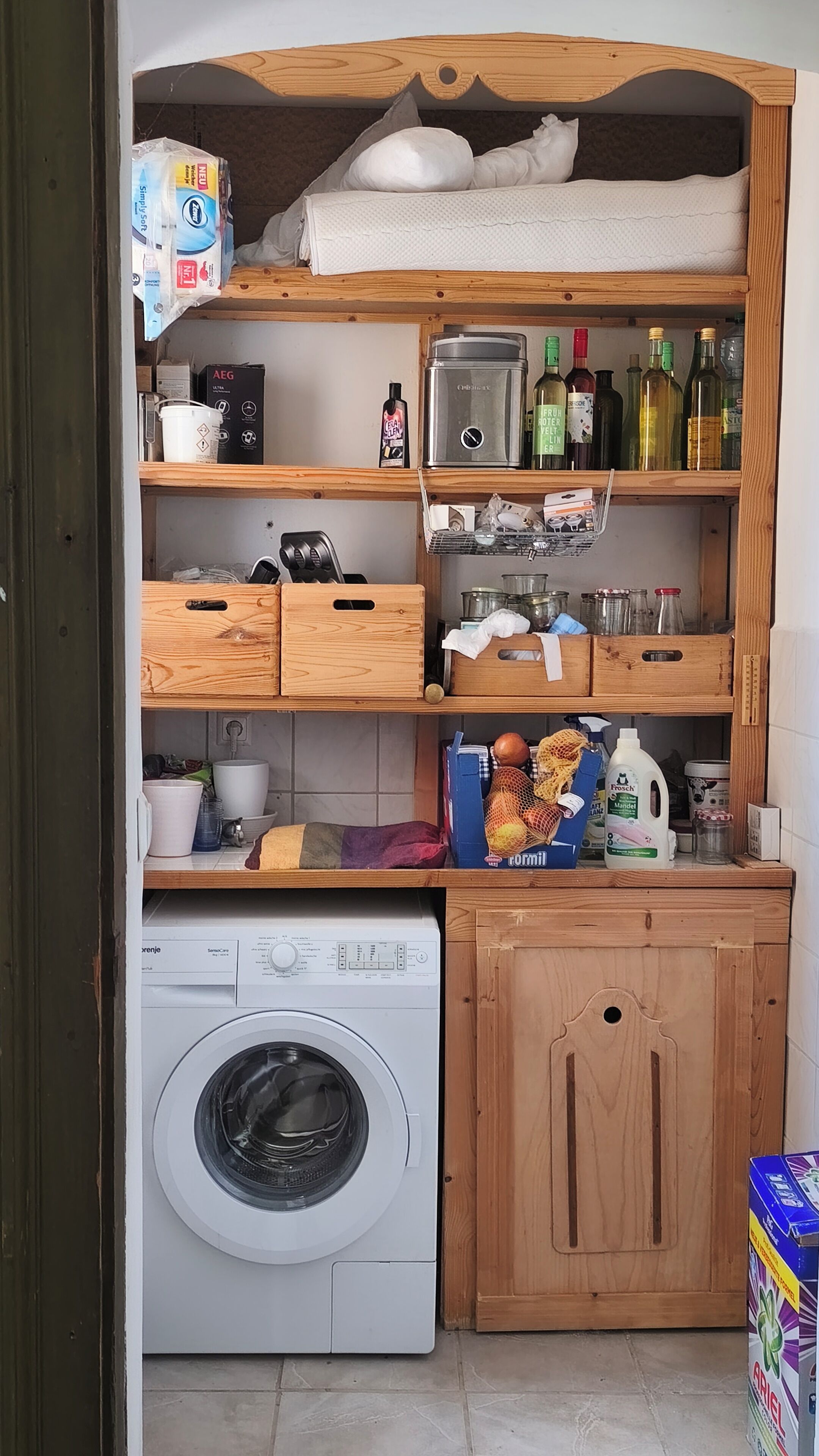 Une cuisine compacte équipée d’un lave-linge, d’étagères en bois et de divers ustensiles de cuisine.