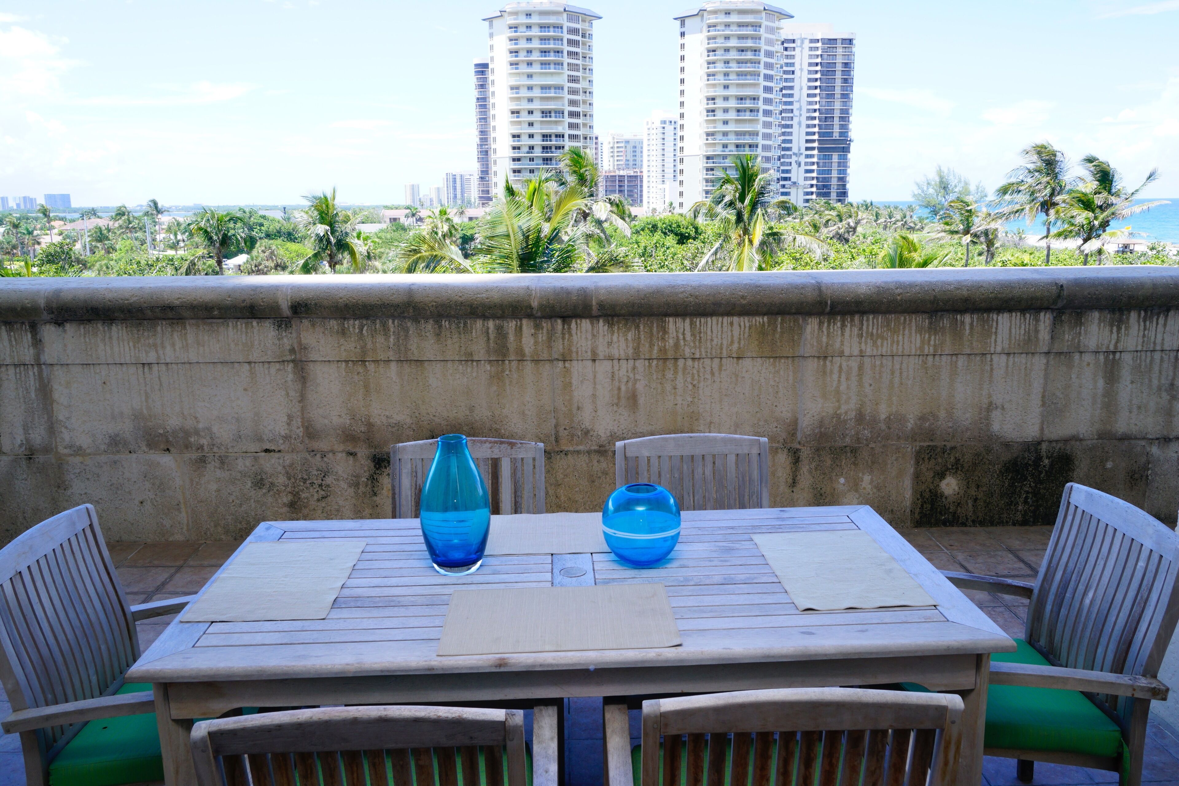 A table with two blue vases, wooden chairs, and a view of palm trees and buildings in the background.