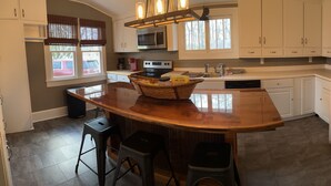A kitchen with white cabinets, a central island with stools, a microwave, oven, and a refrigerator. - The Gray House (Paducah)