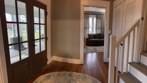 A hallway with a wooden floor, a round rug, a brown door with glass panels, and a staircase with white railings. - The Gray House (Paducah)
