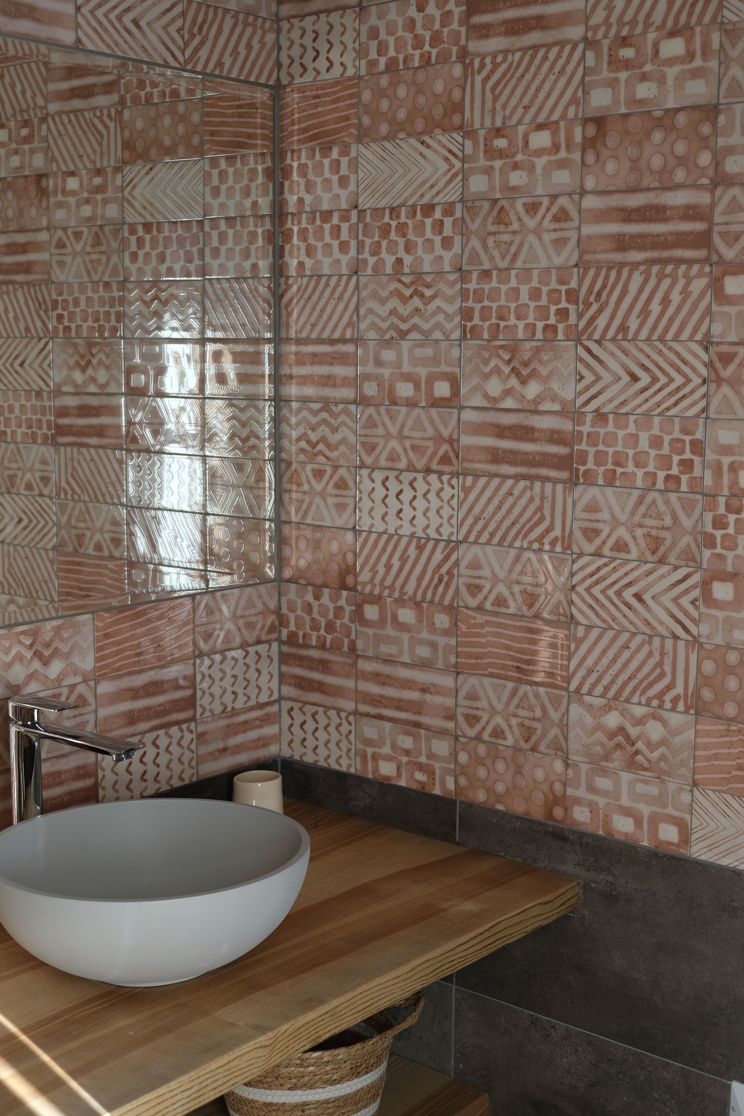 A bathroom with a large white vessel sink, a wooden countertop, and patterned tiles on the walls.
