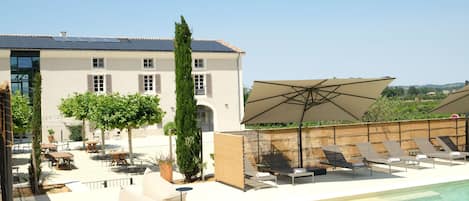 A rooftop pool area with lounge chairs, a large umbrella, and a building with a tiled roof.
