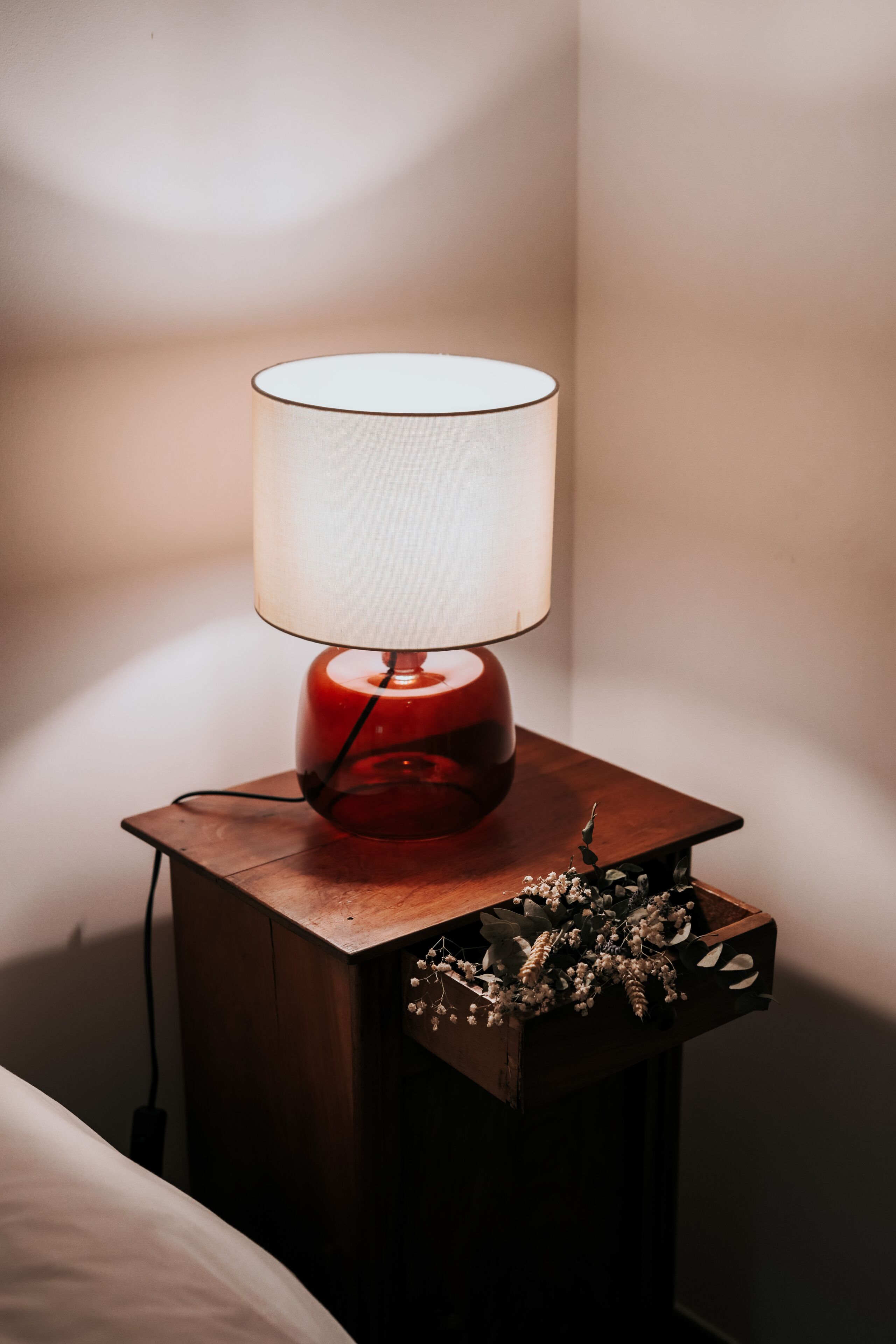 Ein Nachttisch mit roter Lampe und einer dekorativen Schachtel mit Blumen.